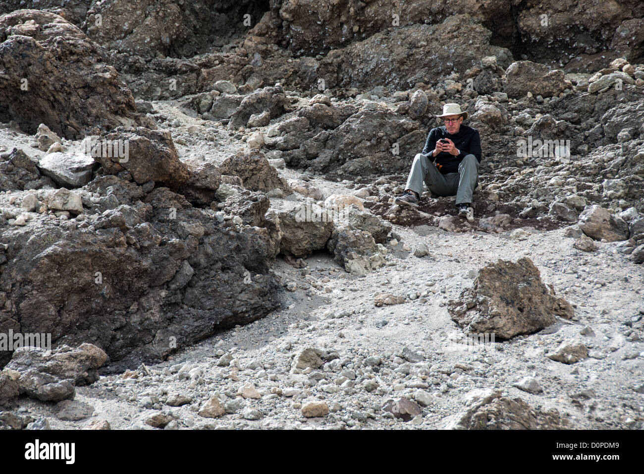 MONTE KILIMANJARO, Tanzania - Un alpinista siede tra le rocce vicino alla cima del monte Kilimanjaro in uno dei rari punti con ricezione cellulare sulla montagna. Foto Stock