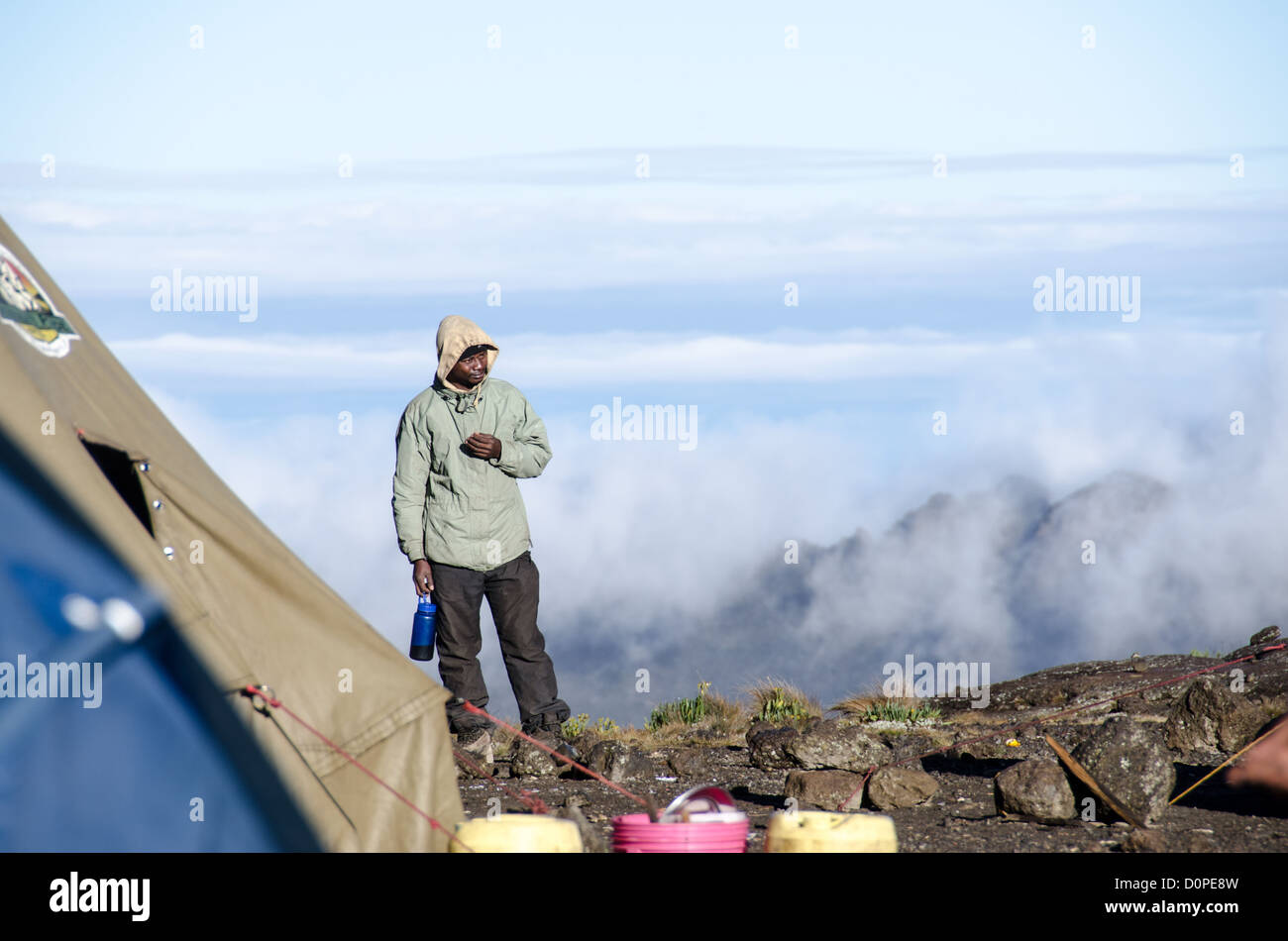 MT KILIMANJARO, Tanzania - un portiere sorge su un bordo roccioso alto sul Monte Kilimanjaro, con le nuvole in background. Foto Stock