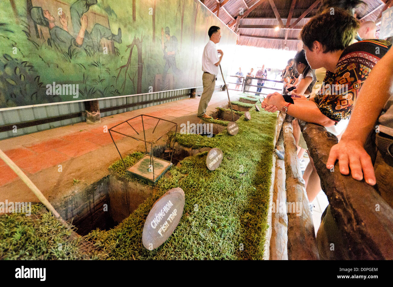 Tunnel di Cu chi trappole di guerra del Vietnam città di ho chi Minh // CITTÀ DI HO CHI MINH, Vietnam - Una guida spiega vari dispositivi anti-personale presso il sito storico dei tunnel di Cu chi, dimostrando le misure difensive utilizzate durante la guerra del Vietnam. La mostra mostra mostra diversi tipi di trappole impiegate per proteggere l'estesa rete di tunnel sotterranei e l'area circostante dalle forze nemiche. Questi manufatti militari conservati fanno parte delle esposizioni educative del sito sulle tattiche difensive vietnamite e sulle strategie di guerriglia. I tunnel di Cu chi, situati a nord-ovest della città di ho chi Minh, serv Foto Stock