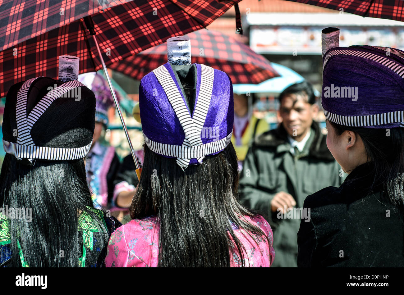 Donne del Capodanno Hmong Copricapi viola Phonsavan Laos | PHONSAVAN, Laos — Giovani donne Hmong indossano copricapi strutturati e colorati e partecipano a un gioco tradizionale di lancio della palla durante il festival del Capodanno post-raccolto. La palla gialla visibile a mezz'aria è usata nel *pov pob*, un rituale di corteggiamento consueto. Poiché la società Hmong impone una rigida esogamia clanica — vietando il matrimonio all'interno dello stesso gruppo di cognomi — questi raduni regionali hanno storicamente offerto ai giovani di villaggi dispersi la principale opportunità di trovare partner idonei. Foto Stock