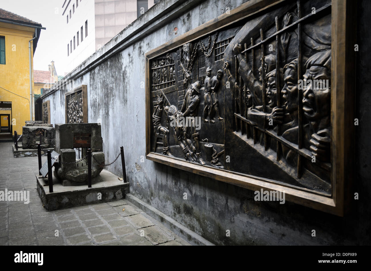 Murale della prigione di Hoa lo raffigurante gli abusi dei prigionieri di Hanoi Vietnam // HANOI, Vietnam - a destra e in lontananza, montati sul muro, sono presenti murales in bronzo che raffigurano le dure condizioni per i prigionieri della prigione di Hoa lo sotto il dominio coloniale francese. A sinistra c'è un esempio del piccolissimo tunnel di drenaggio attraverso il quale diversi prigionieri sono fuggiti. La prigione di Hoa lo, nota sarcasticamente come Hanoi Hilton durante la guerra del Vietnam, era originariamente una prigione coloniale francese per prigionieri politici e poi una prigione nordvietnamita per prigionieri di guerra. È particolarmente famosa per essere la prigione usata per gli americani Foto Stock