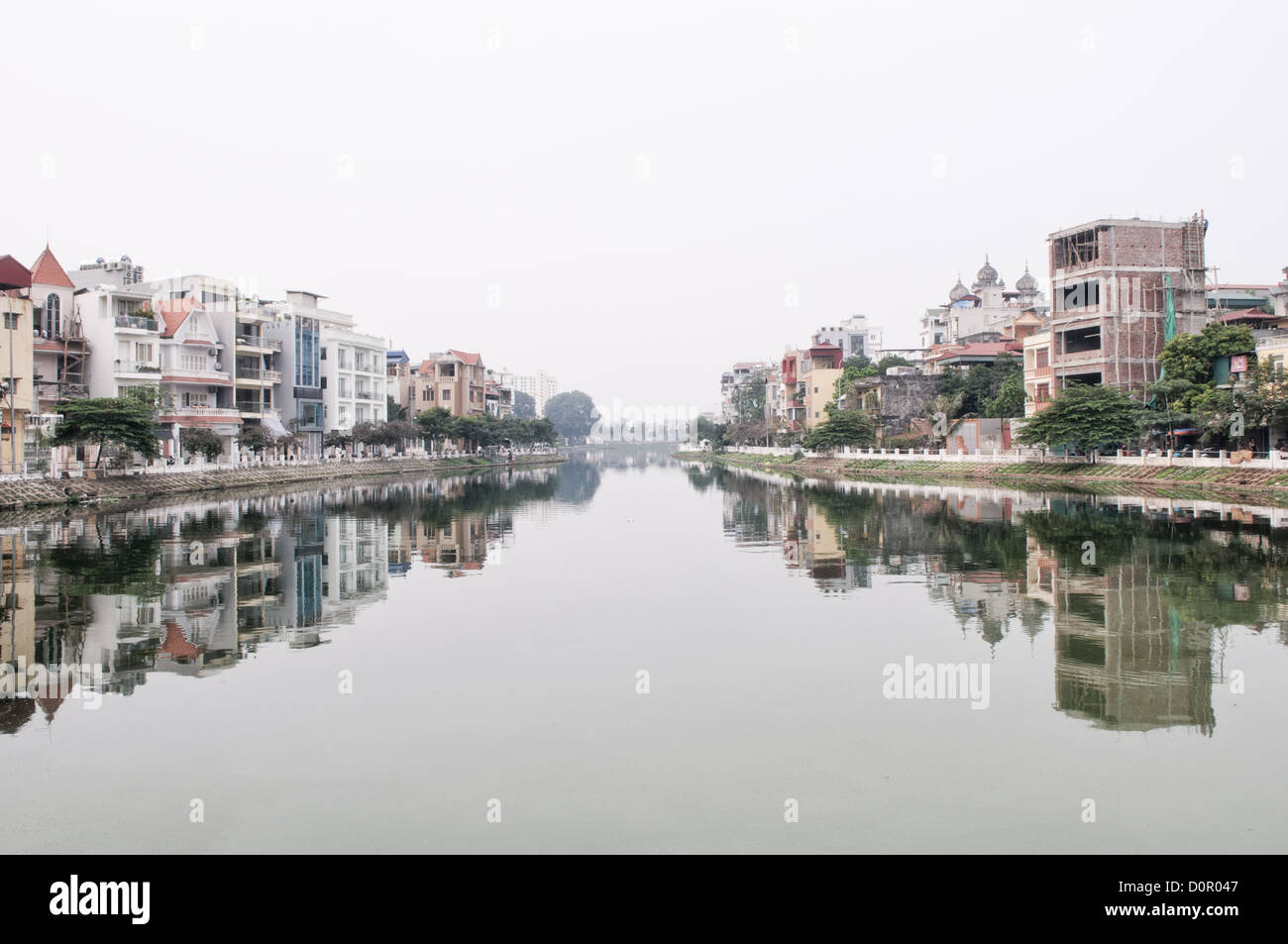 HANOI, Vietnam - Un canale nel Lago Ovest (Ho Tay) ad Hanoi, Vietnam, con case e appartamenti sulla banca o riflessa su acque calme. Foto Stock