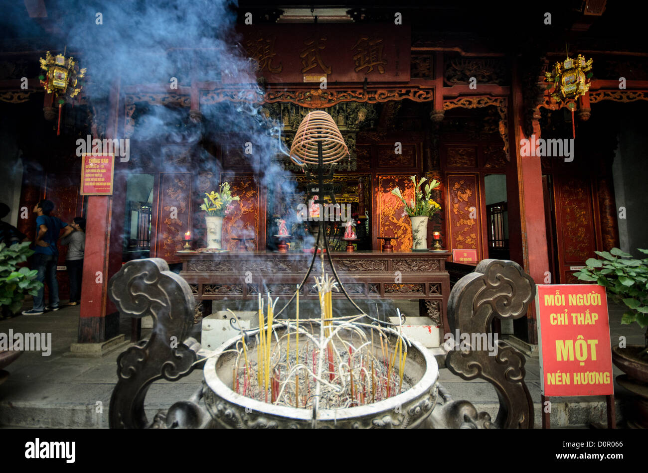 Tempio di Quan Thanh Incense Hanoi Vietnam // HANOI, Vietnam - fumo blu proveniente dalla combustione di incenso che si diffonde attraverso l'aria fuori dal tempio di Quan Thanh ad Hanoi. Il tempio taoista risale all'XI secolo e si trova vicino al Lago Ovest, nello storico quartiere di Ba Dinh. Il tempio di Quan Thanh è dedicato a Tran Vo, una divinità della religione popolare vietnamita, e rimane un luogo di culto attivo. Il tempio è uno dei quattro templi sacri di Hanoi, costruiti per proteggere l'antica capitale dagli spiriti maligni secondo le credenze tradizionali. La combustione dell'incenso è una pratica rituale centrale a Vietname Foto Stock