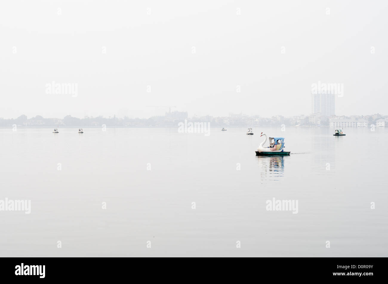 HANOI, Vietnam - le barche a pale modellate come cigni galleggiano sulle calme acque del Lago Occidentale (ho Tay) ad Hanoi, Vietnam, in una giornata nebbiosa. Foto Stock