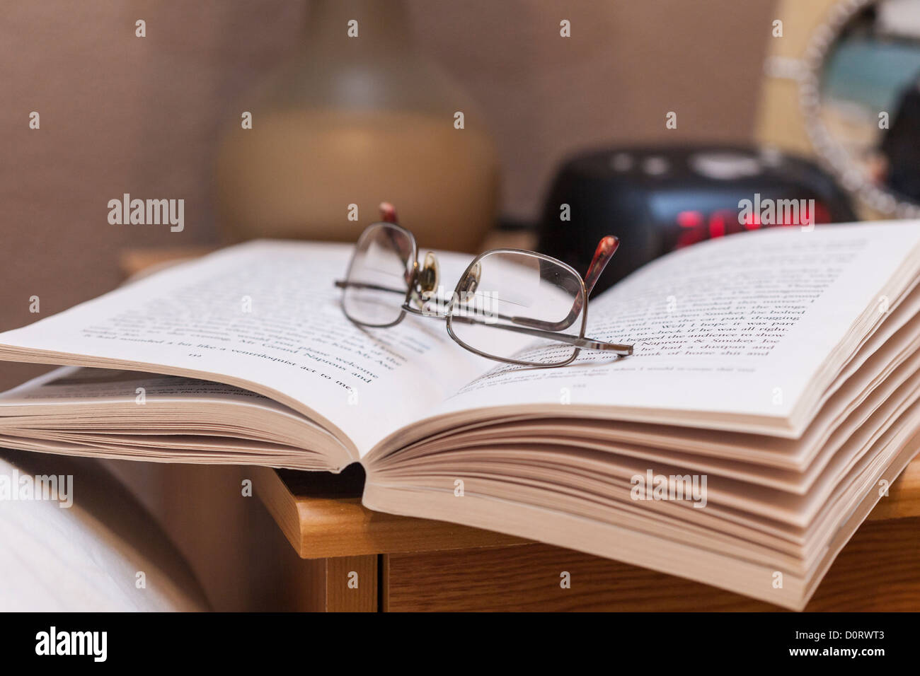 Notte Tempo di lettura, lettura a letto. Libro in brossura con gli occhiali da lettura sul comodino. Foto Stock
