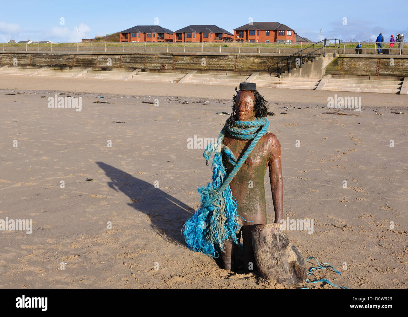 L'uomo del ferro su Crosby beach sorge guerriero vestito di moda in flotsam raccolte dalla spiaggia Foto Stock