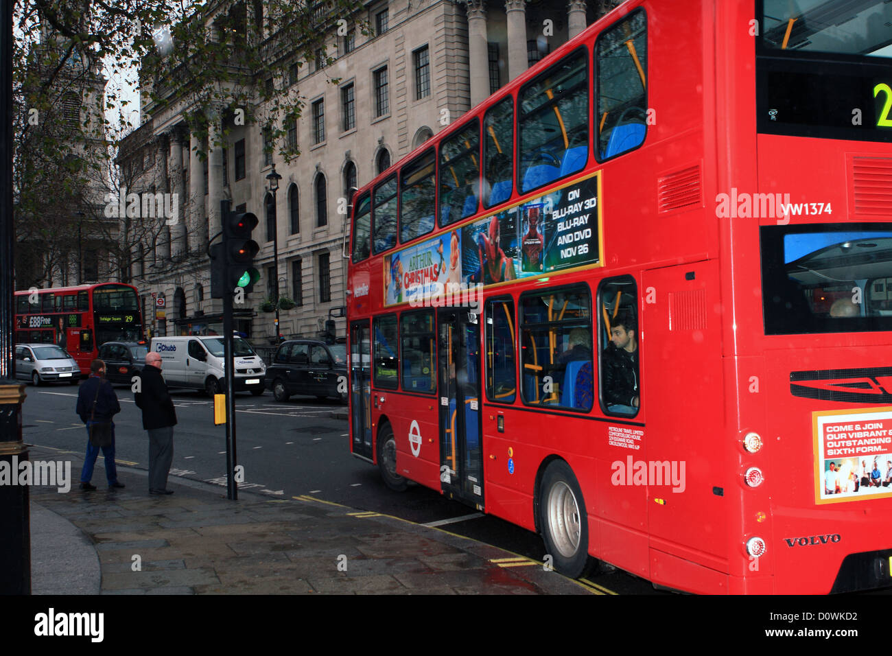 Un rosso London double decker bus passando verde semaforo mentre due persone attendere per attraversare la strada. Foto Stock