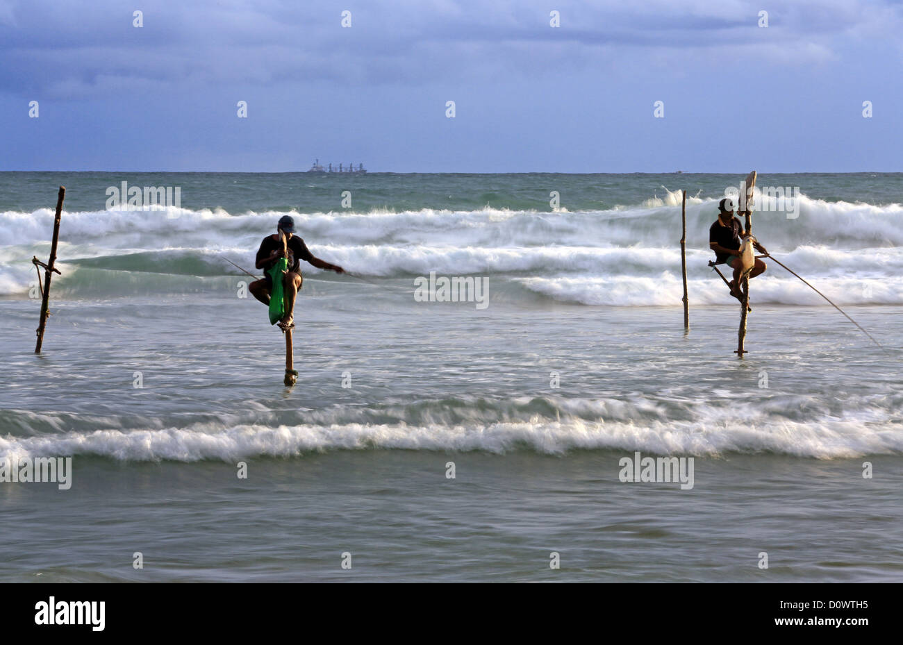 Stilt tradizionali pescatori la cattura di sardine tra grandi surf in Koggala, Sri Lanka. Foto Stock