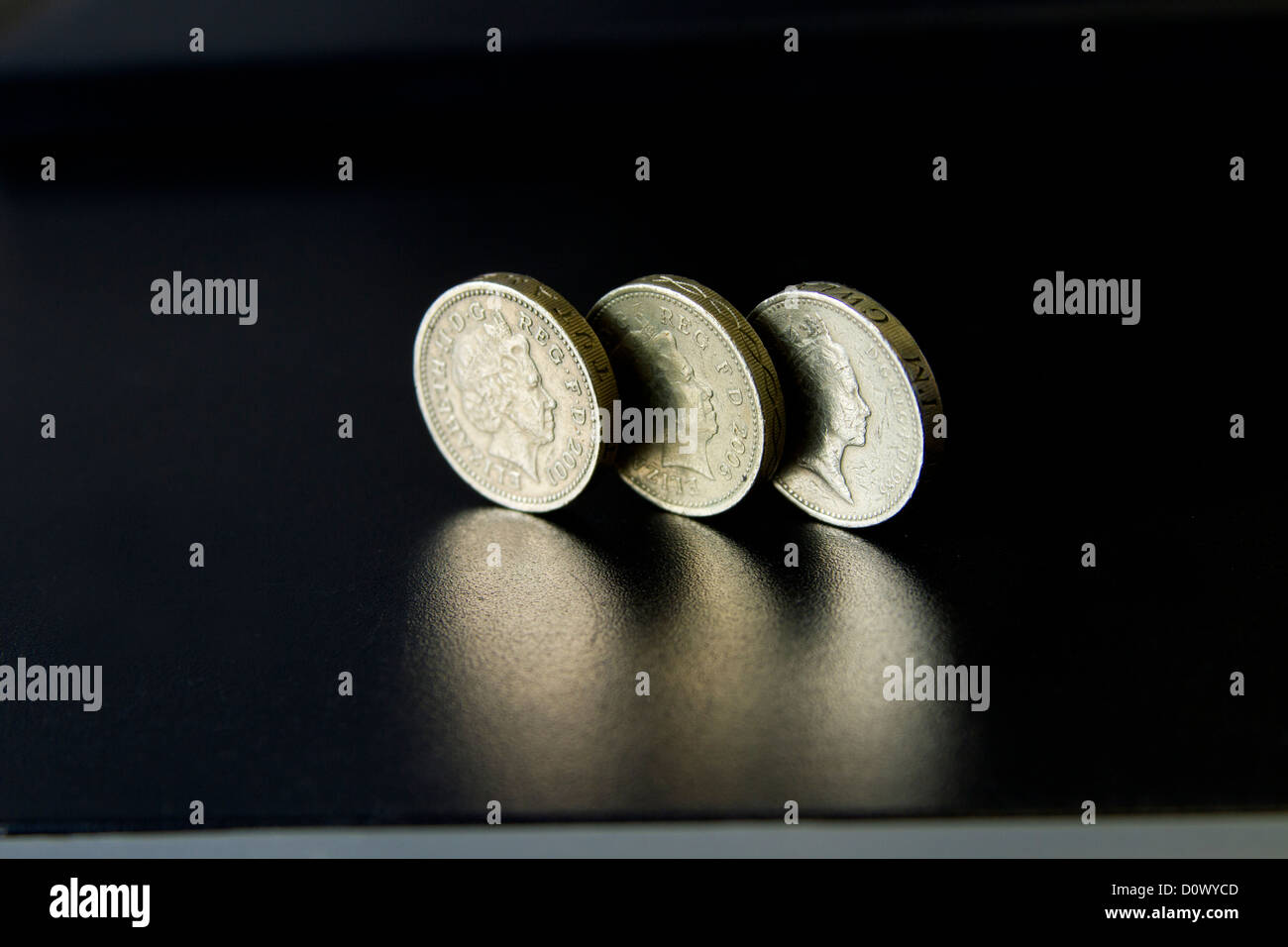 Libbra moneta di sterlina tre monete lucido getto ombra sulla superficie nera riflettente sul tavolo scrivania per servizi bancari e finanziari Foto Stock