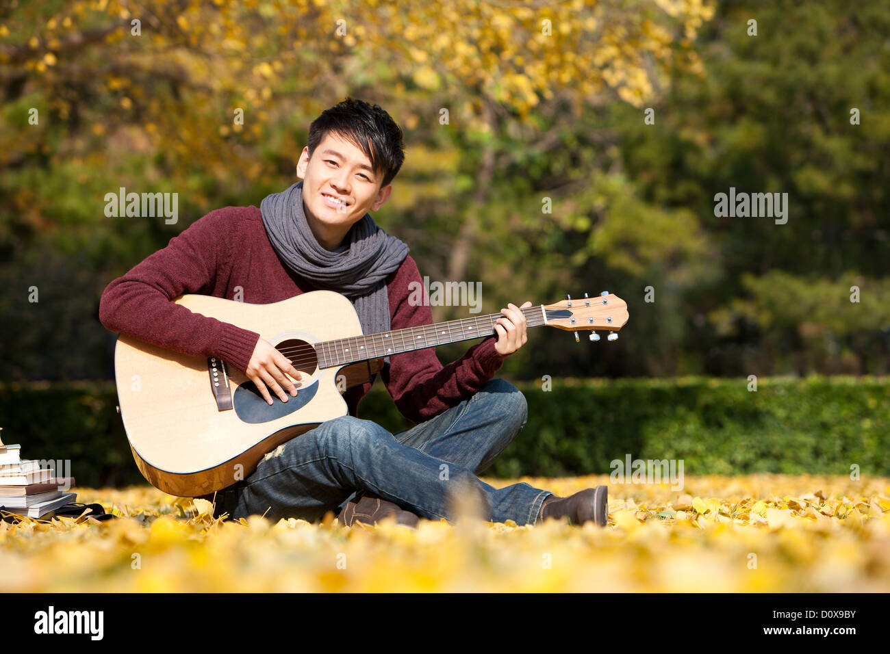 Collegio maschile studente con la chitarra e libri godendo il clima piacevole in autunno Foto Stock