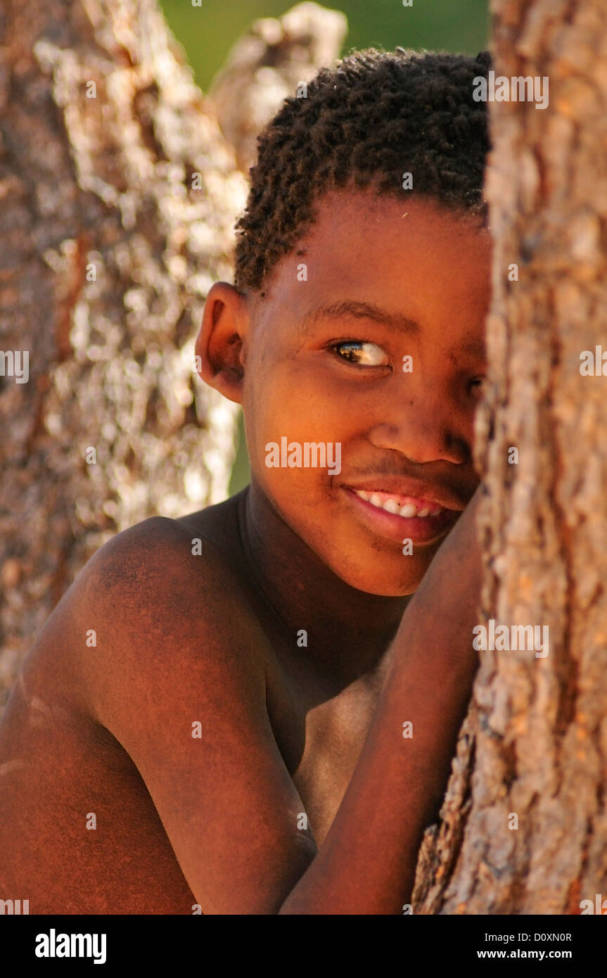Africa i Boscimani della Namibia ritratto dietro tree bambino nascondendo clan di cacciatori-raccoglitori nomadi naturale primitiva sorridente Foto Stock