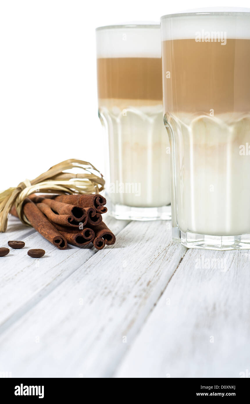 Latte macchiato in un bicchiere con i chicchi di caffè e bastoncini di cannella Foto Stock