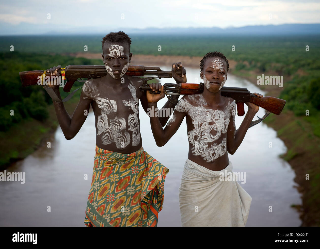 Karo tribù ragazzi con verniciatura scocca e ponendo Kalachnikovs oltre il fiume Omo Korcho Village, Valle dell'Omo, Etiopia Foto Stock