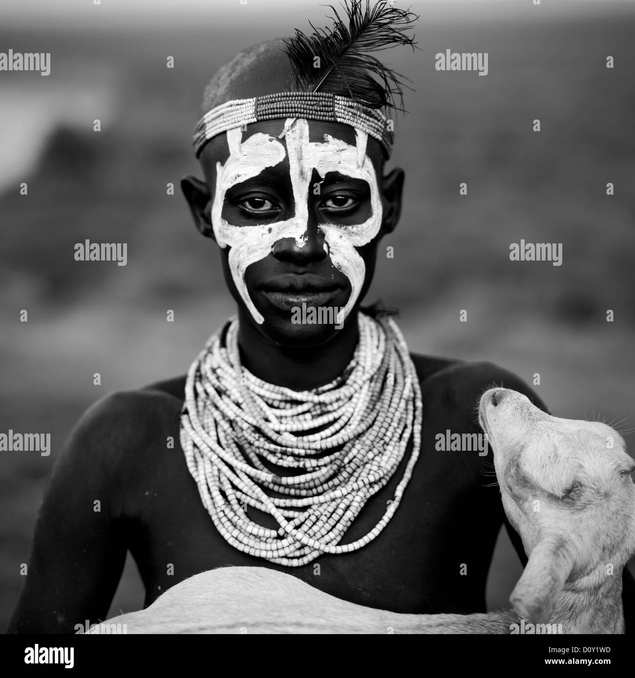 Ritratto in bianco e nero di un Karo Tribe Uomo con faccia dipinta tenendo una capra nelle sue braccia, Korcho Village, Valle dell'Omo, Etiopia Foto Stock