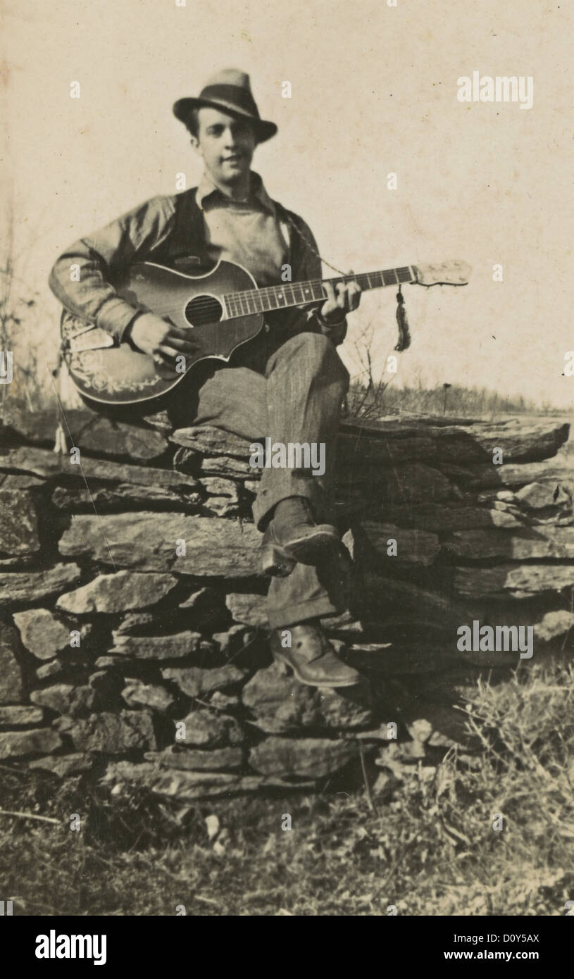 Circa 1910s fotografia, uomo di suonare una chitarra su un muro di pietra, probabilmente la Nuova Inghilterra, Stati Uniti d'America. Foto Stock