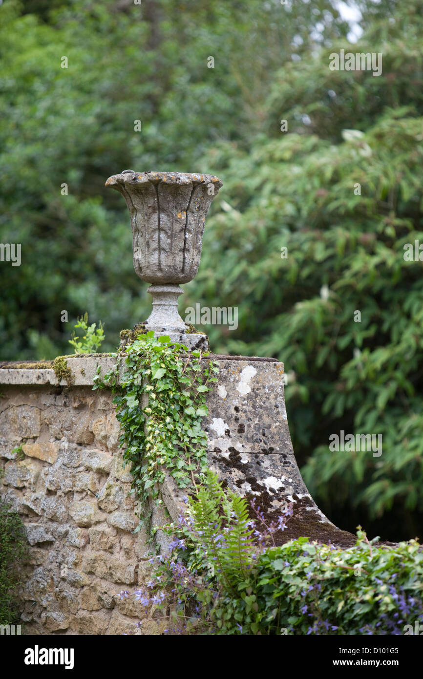 In pietra antica urna di piante sul muro del giardino, Gloucestershire, England, Regno Unito Foto Stock