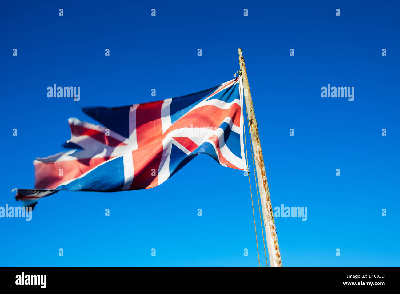 Ragged, lacerato e trascurato Union Jack, il British bandiera nazionale, su un palo di bandiera contro un cielo blu chiaro. Foto Stock