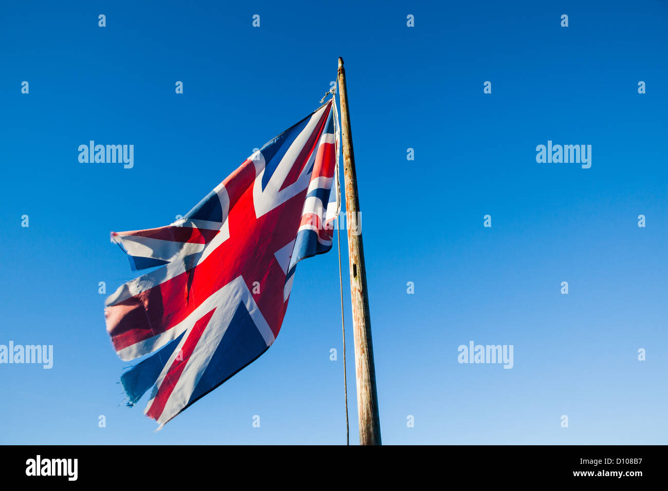 Ragged, lacerato e trascurato Union Jack, il British bandiera nazionale, su un palo di bandiera contro un cielo blu chiaro. Foto Stock