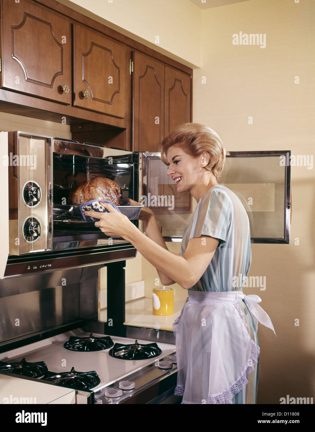 Anni sessanta donna casalinga nel grembiule la cottura in forno per la  cottura arrosto IN CUCINA Foto stock - Alamy