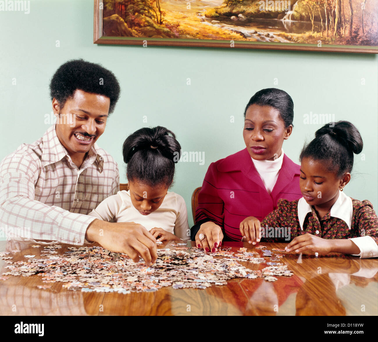 Anni Settanta afro-americano della famiglia uomo donna madre padre di due bambini ragazze seduta tabella facendo Jigsaw Puzzle Retrò Foto Stock