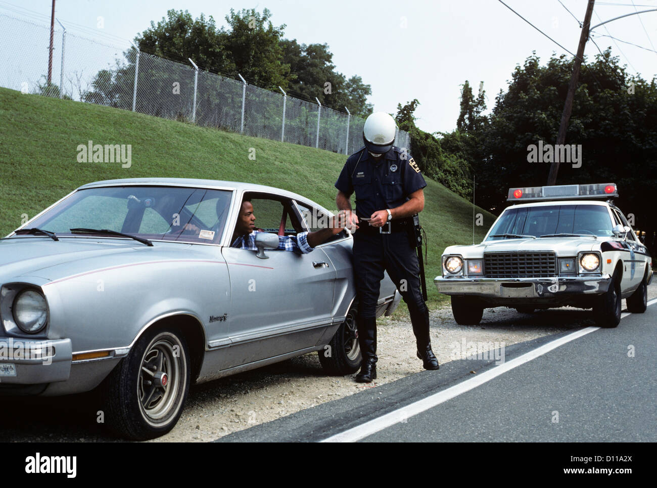 Anni Settanta funzionario di polizia CONTROLLO PATENTE di afro-AMERICAN DRIVER SUL LATO DELLA STRADA Foto Stock