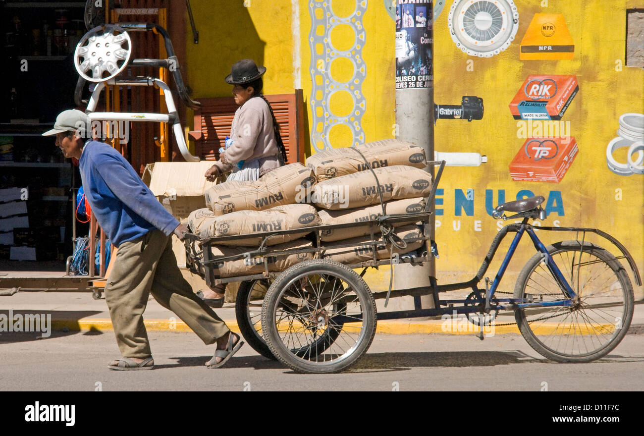 L'uomo tirando bicicletta carrello carico di sacchi di cemento lungo una strada della città di Puno, Perù Sud America Foto Stock