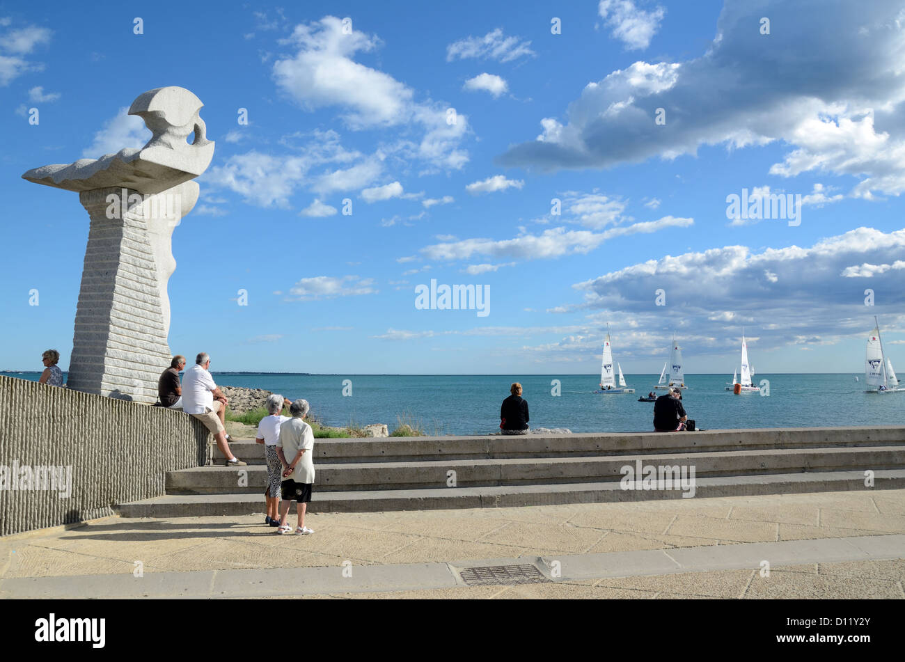 Turisti e scultura pubblica sulla passeggiata fronte mare o sul lungomare della località turistica di la Grande-Motte Hérault Francia Foto Stock