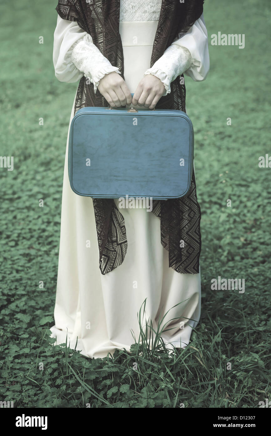 Una donna con un marrone scialle e una valigia blu Foto Stock