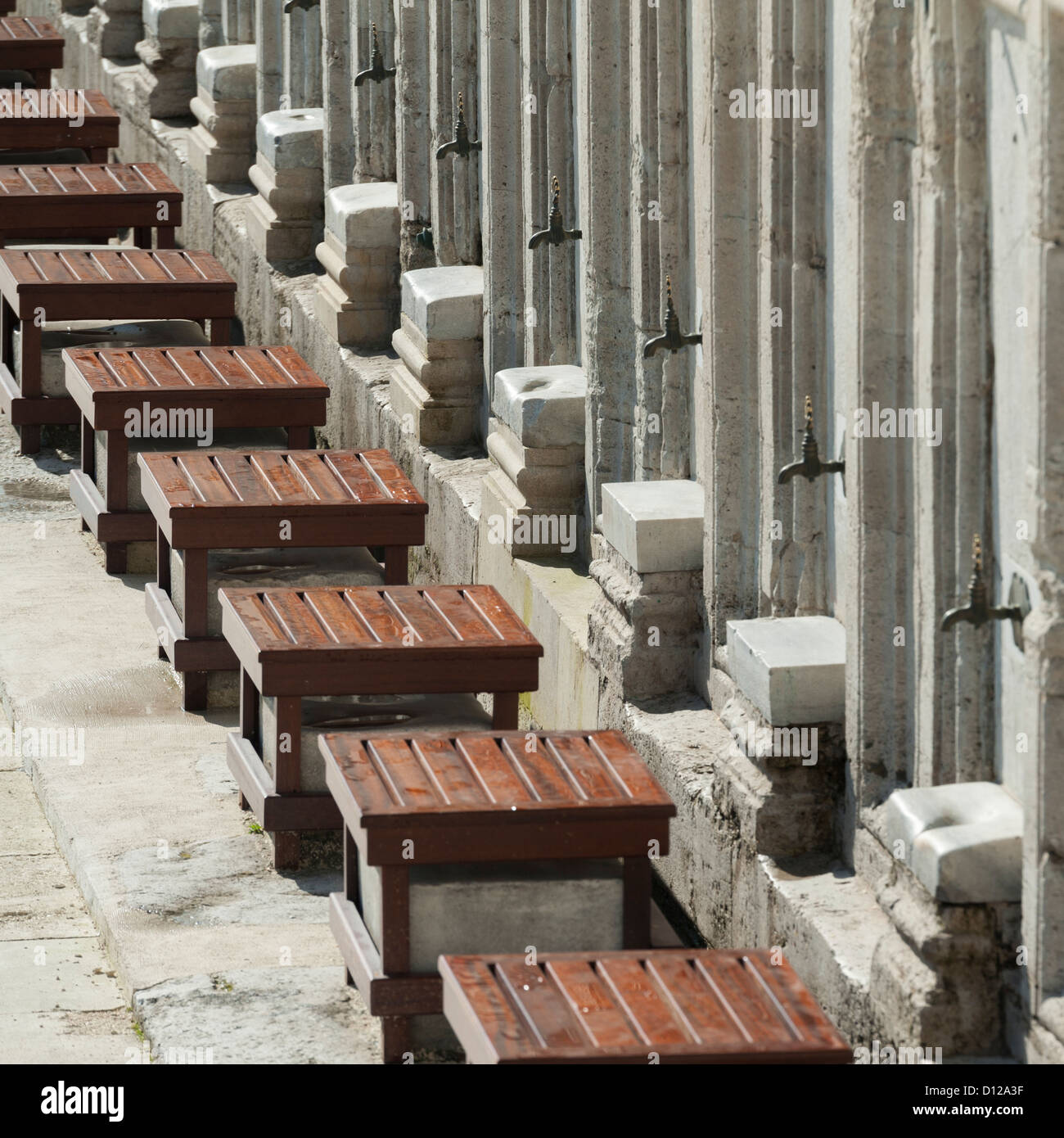 Posti a sedere in legno sotto Rubinetti di acqua in una fila lungo una parete presso la Moschea di Suleymaniye; Istanbul Turchia Foto Stock