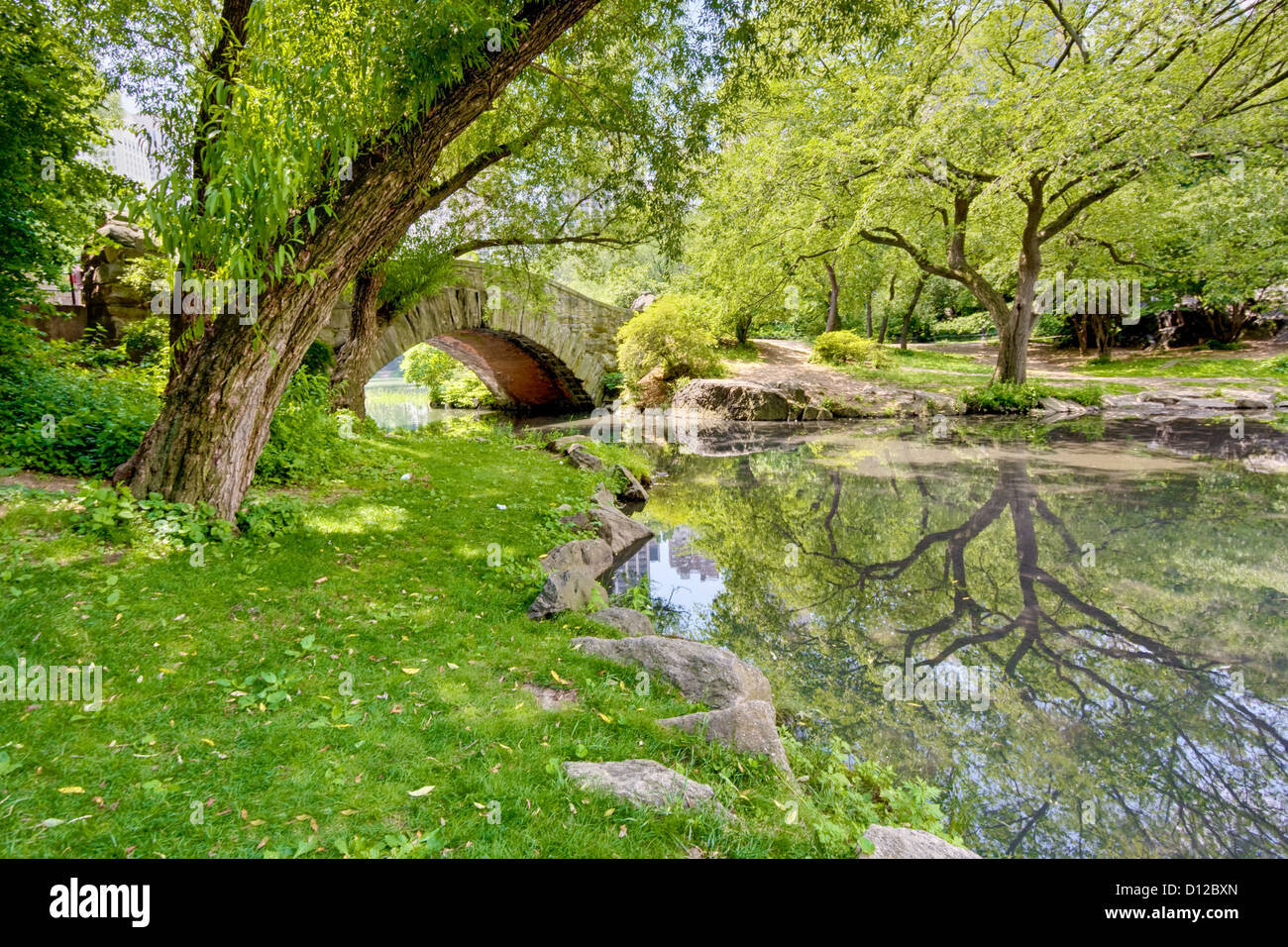 Un ponte in pietra a Central Park, NY. Vi è un grande albero e riflesso nello stagno che corre sotto il ponte. Foto Stock