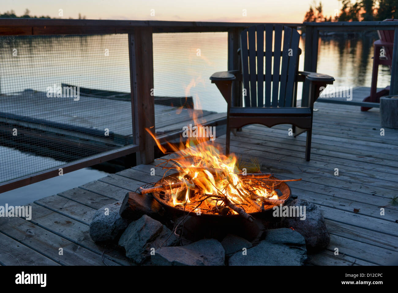 Una buca per il fuoco su una banchina in legno su un lago al tramonto; Lago di boschi Ontario Canada Foto Stock