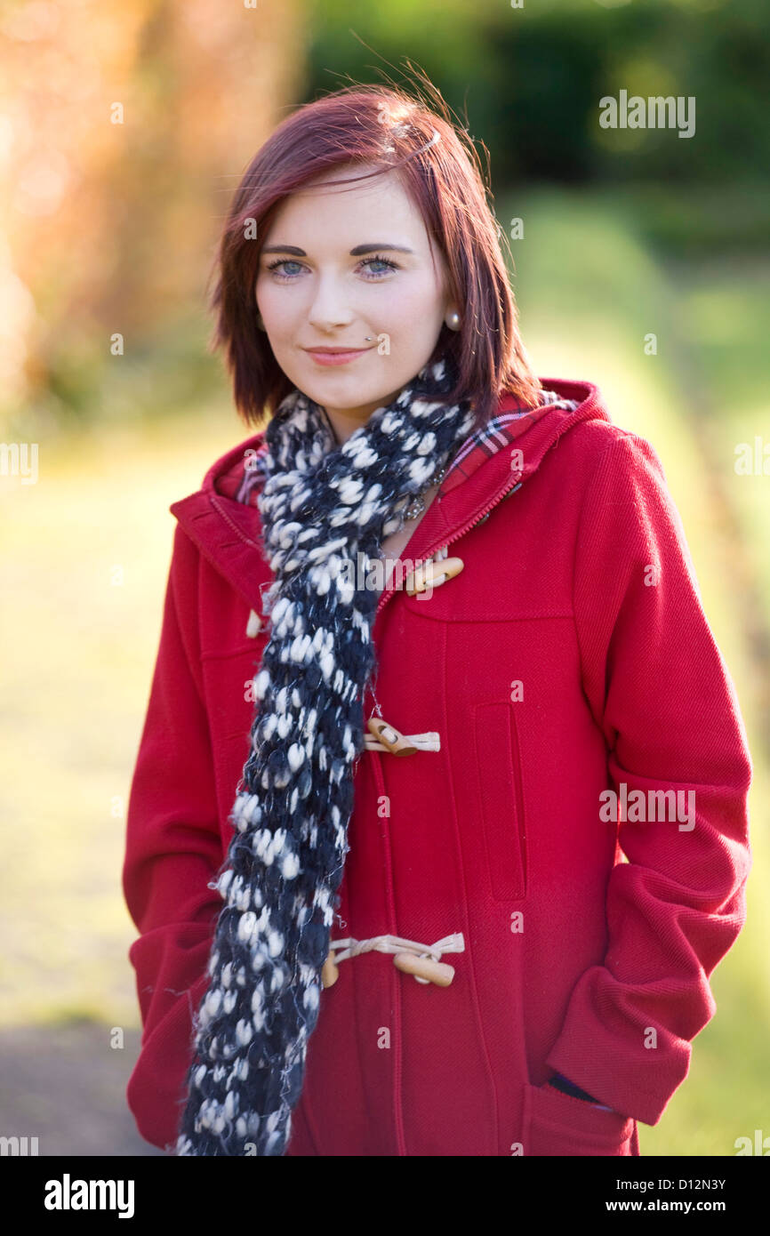 Giovane donna che indossa un cappotto rosso in un parco in Scozia. Foto Stock