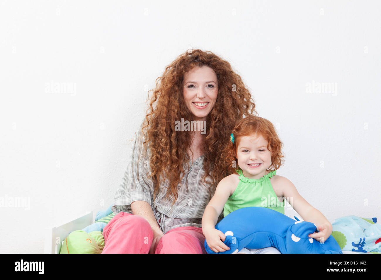 Germania Berlino, madre e figlia seduta sul letto, sorridente, ritratto Foto Stock
