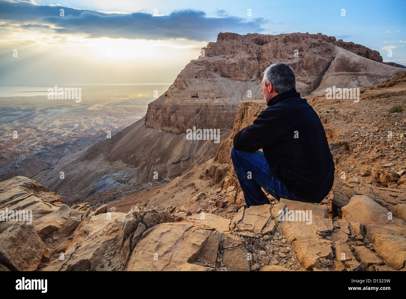 Un uomo si siede su una roccia che guarda oltre il deserto della Giudea; Israele Foto Stock