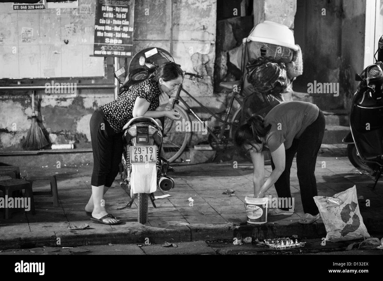 Due donne un piegato su un ciclomotore in chat con il Street nella città vecchia di Hanoi e di notte Foto Stock
