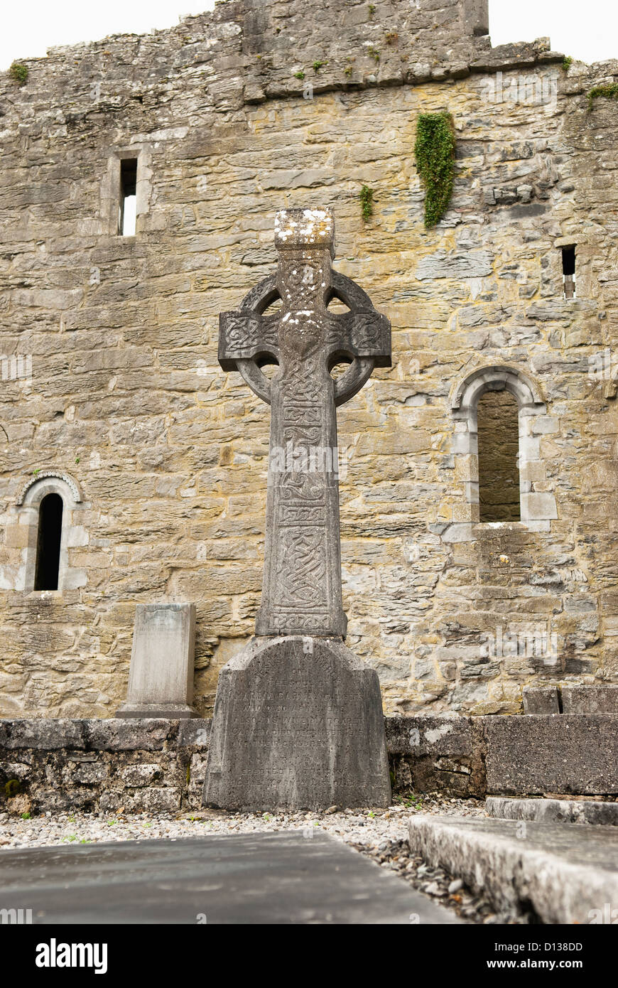 Una grande croce celtica monumento davanti alle rovine di un edificio in pietra; Irlanda Foto Stock