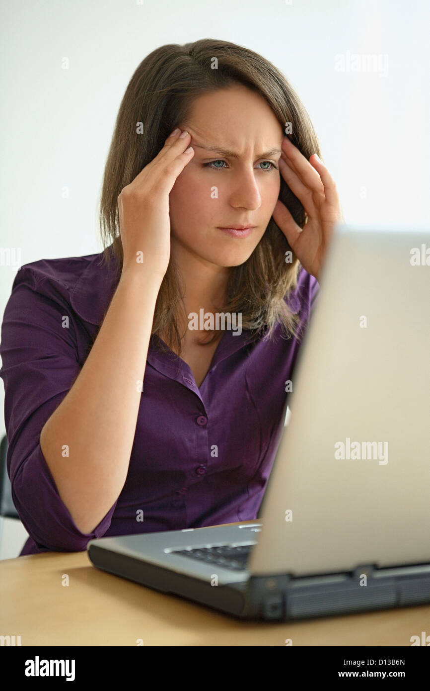 In Germania, in Baviera, Monaco di Baviera, giovane donna con mal di testa lavorando sul computer portatile Foto Stock