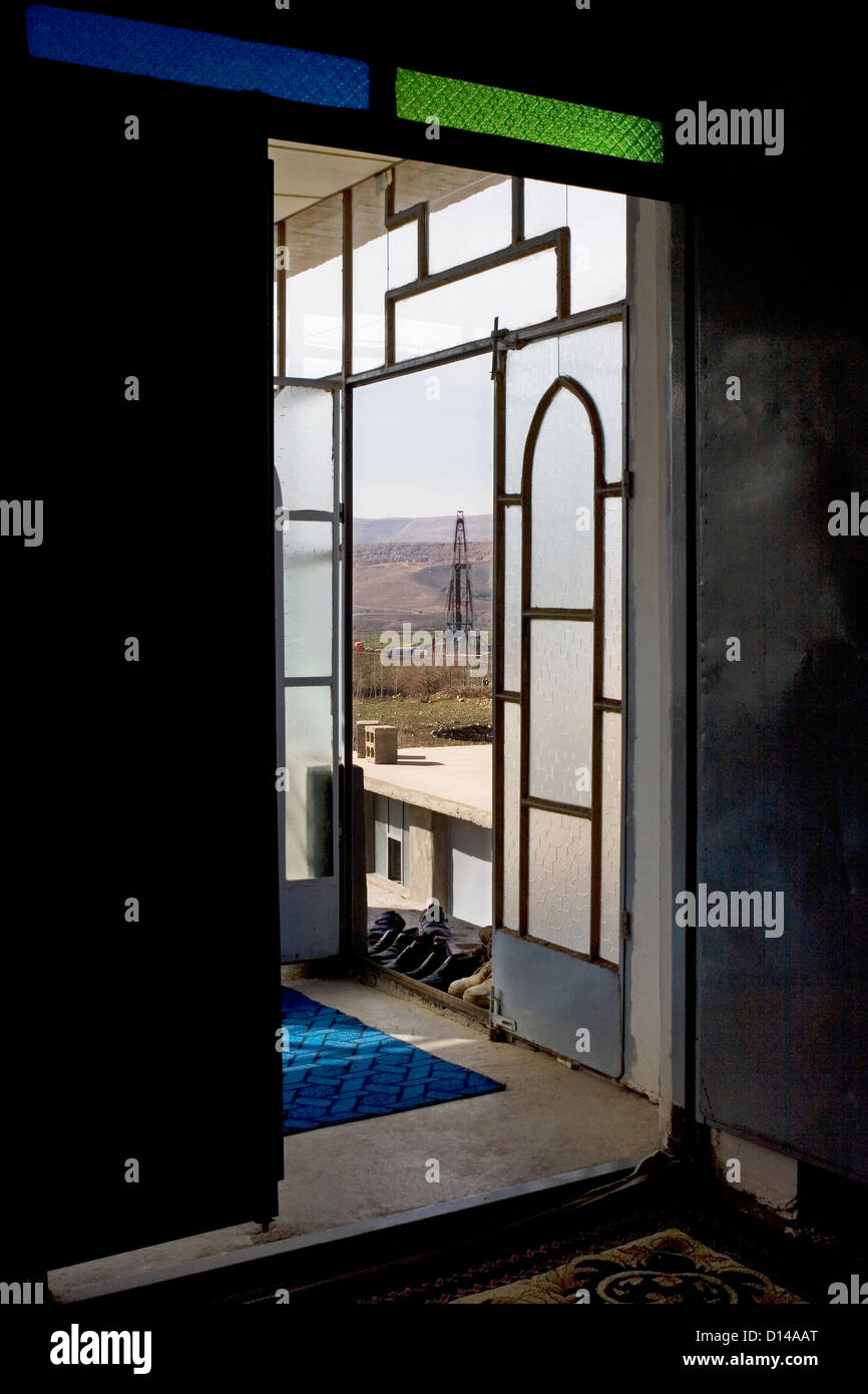 Attraverso la porta di ingresso al Villaggio Copala Moschea, con olio di esplorazione di gas rig bene nel vicino a distanza al di fuori, Kurdistan iracheno, Iraq Foto Stock