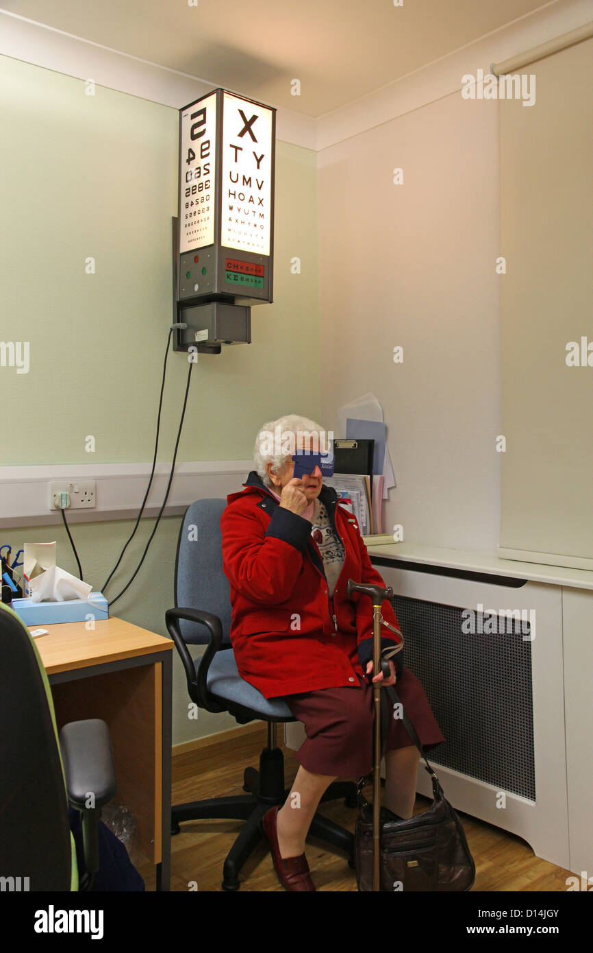 Una vecchia donna avente i suoi occhi testati per la cataratta la lettura di un occhio tabella di dati di prova Foto Stock