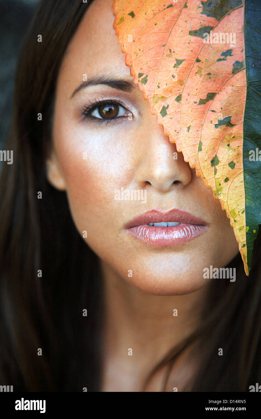 Hawaii, Oahu, primo piano della giovane femmina di bellezza Headshot con foglie colorate accanto al suo volto. Foto Stock