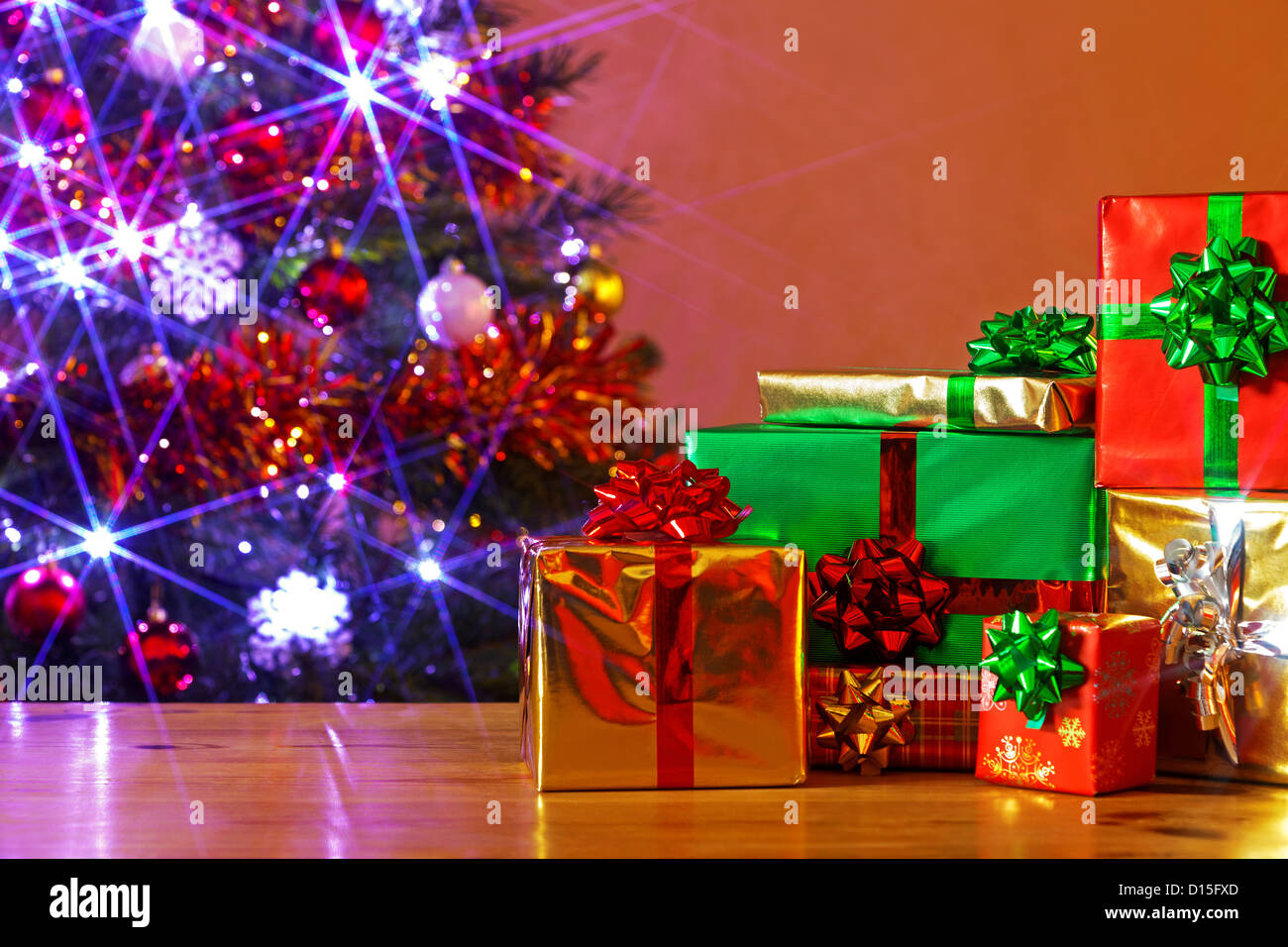 Gift Wrapped regali di Natale su una tavola e un decorate albero dietro con fata luci accese, Foto Stock