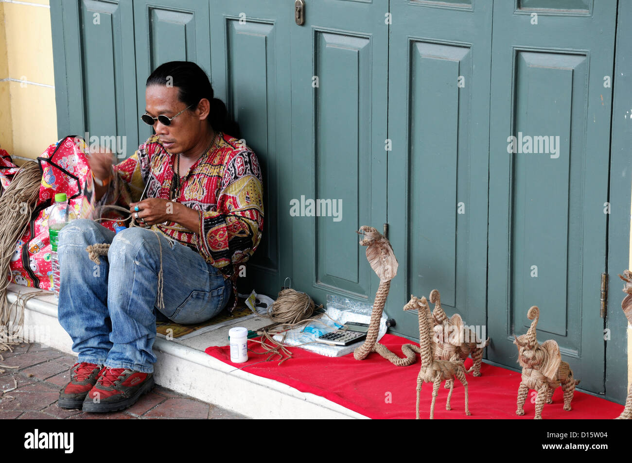 L'uomo la tessitura rendendo la creazione di canapa sagomato di forma animali elefante giraffa cobra street venditore mercato Tailandia Bangkok vendita souvenir Foto Stock