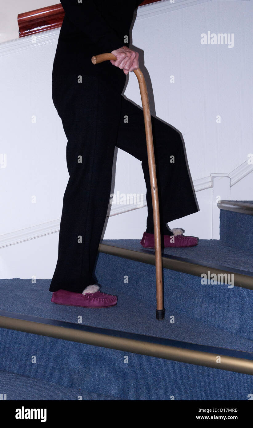 Signora anziana a salire le scale con un bastone da passeggio, Dorset, Regno Unito. Europa Foto Stock