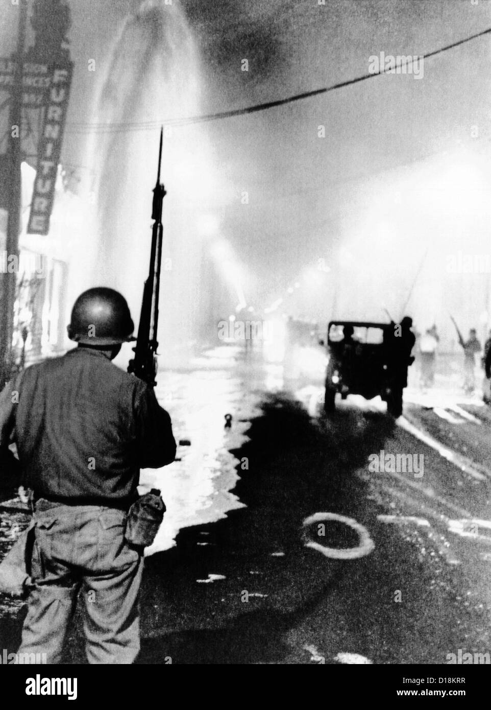 La Guardia Nazionale in watt durante la gara 1965 sommossa. I detriti cucciolate le strade e un geyser da broken idrante di fuoco spray a Foto Stock