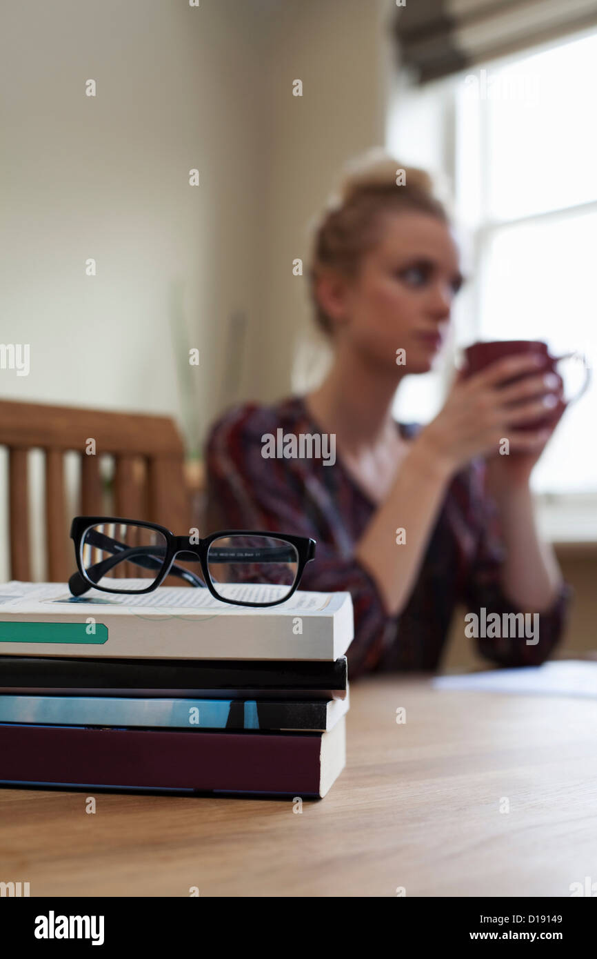 Libri e coppia di bicchieri in primo piano, giovane donna con la tazza di caffè in background Foto Stock