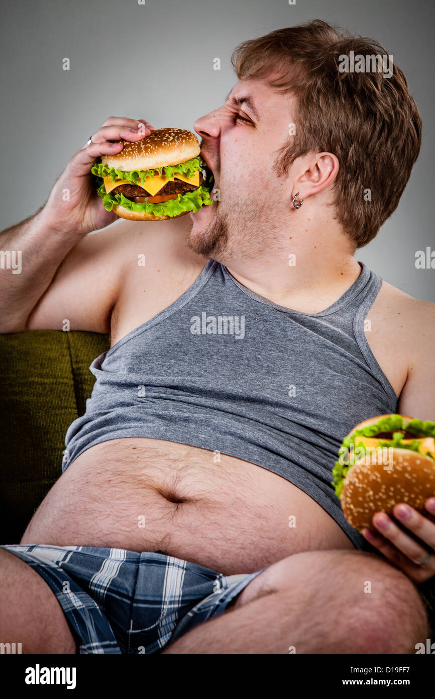 Fat Man mangiare hamburger seduti sulla poltrona Foto Stock