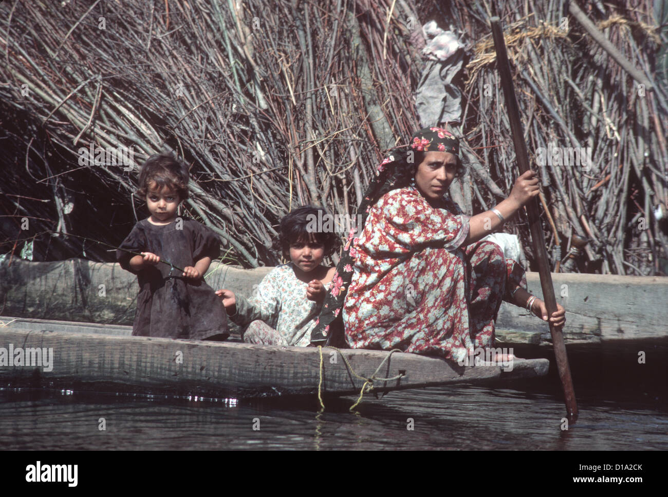 Il Kashmir, fiume Jhelum - donna le piastre a fondo piatto barca in legno con due bambini piccoli Foto Stock