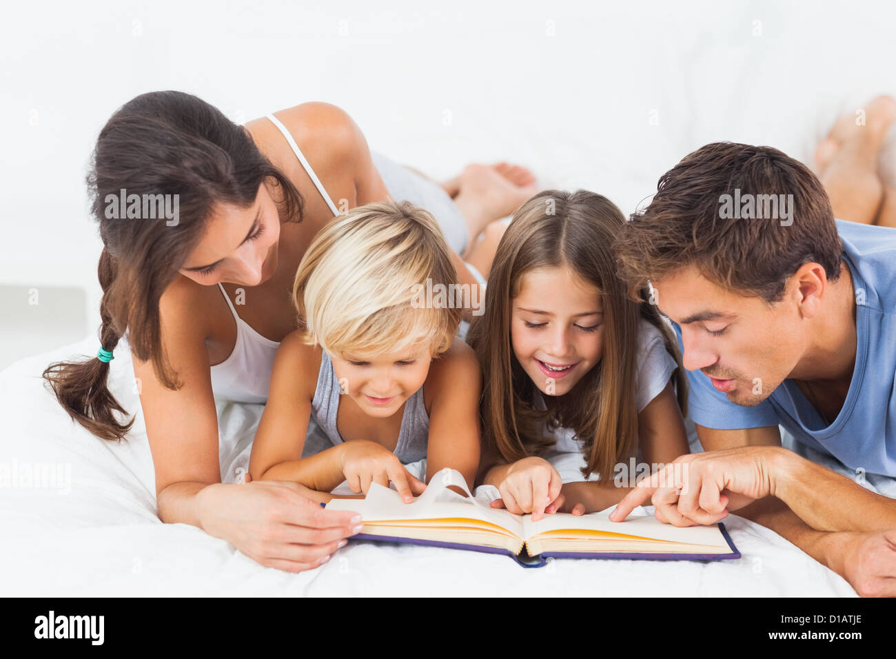 Famiglia a leggere un libro sul letto Foto Stock