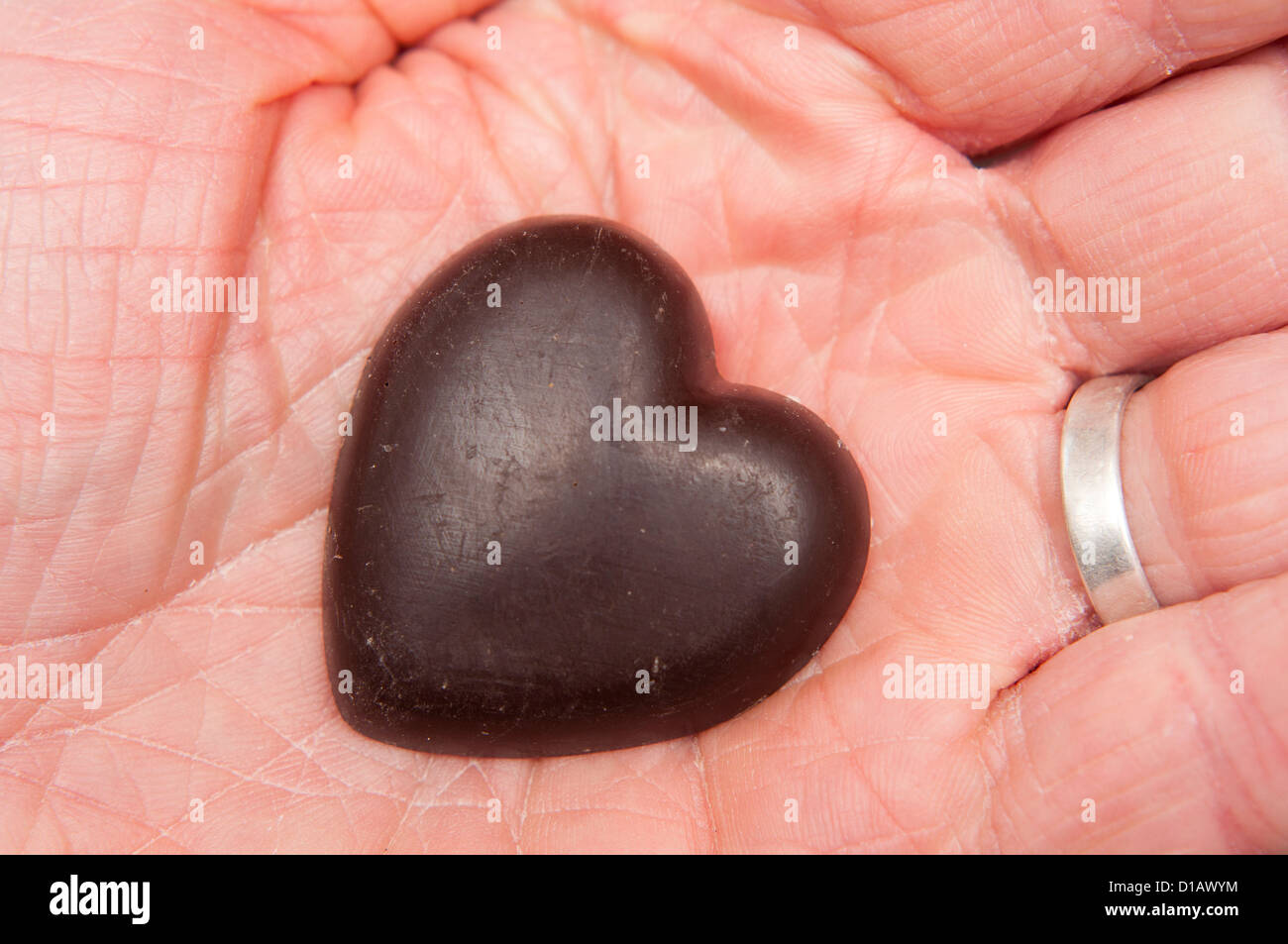 Il cioccolato forma di cuore nel palmo di una mano di un uomo con anello di nozze. Foto Stock