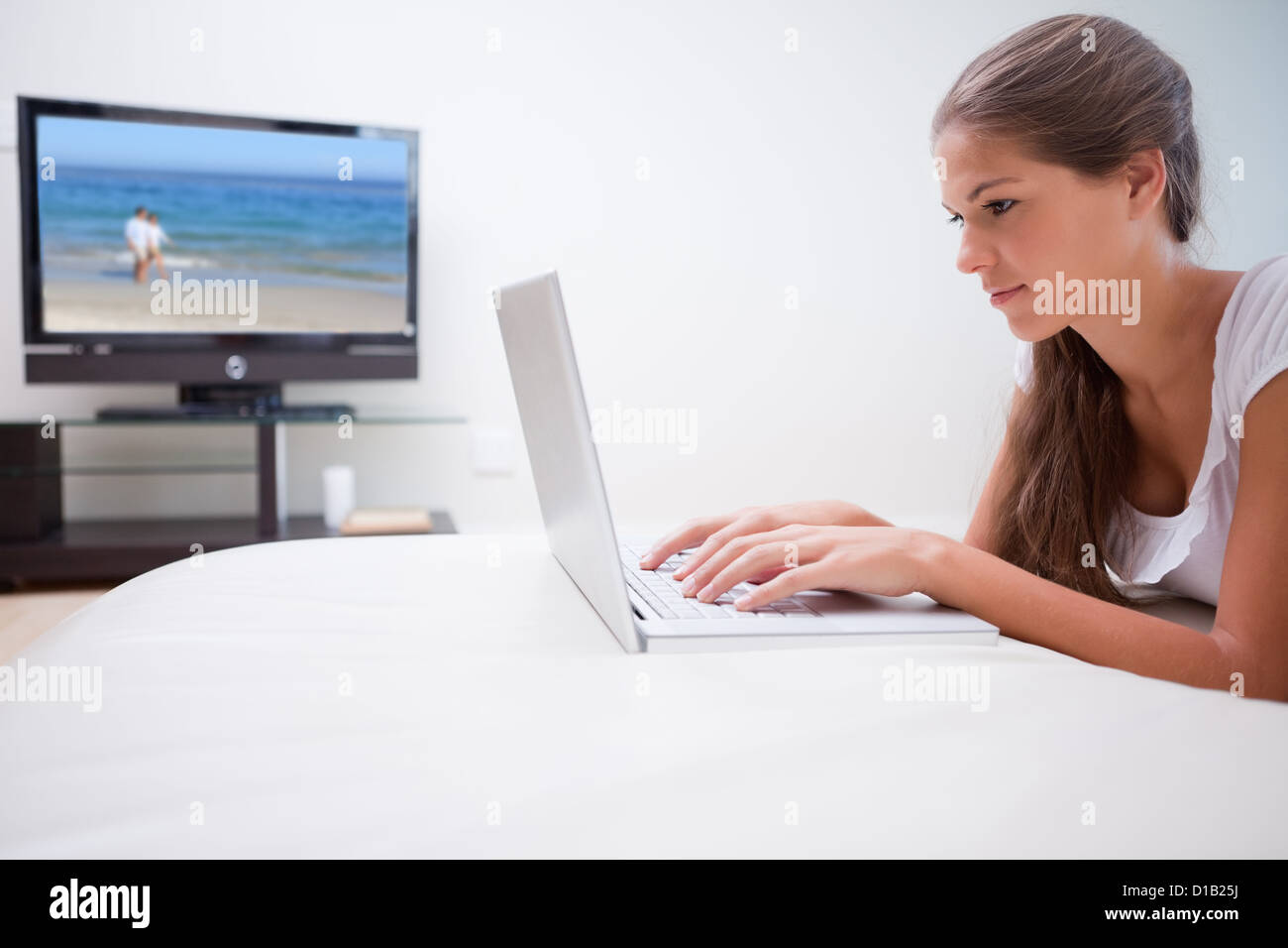 Donna sul suo computer portatile con televisione in background Foto Stock